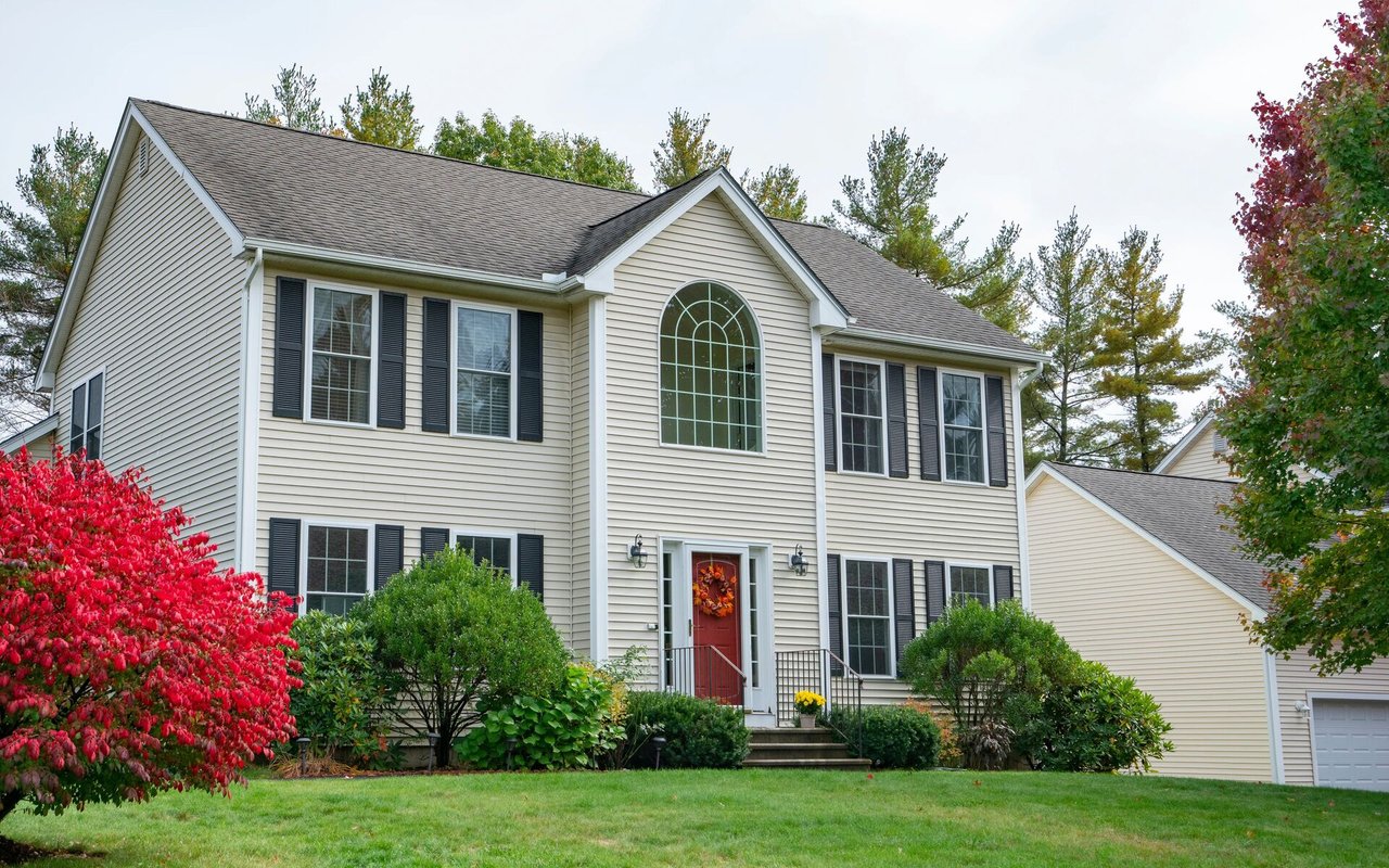 Two-story suburban house with an arched window, red front door, and autumn shrubs.