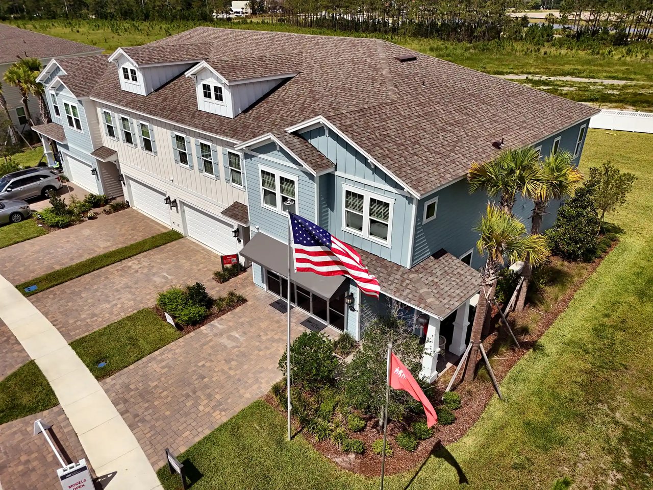 Blue-gray two-story building with dormers, palm trees, and an American flag flying out front.