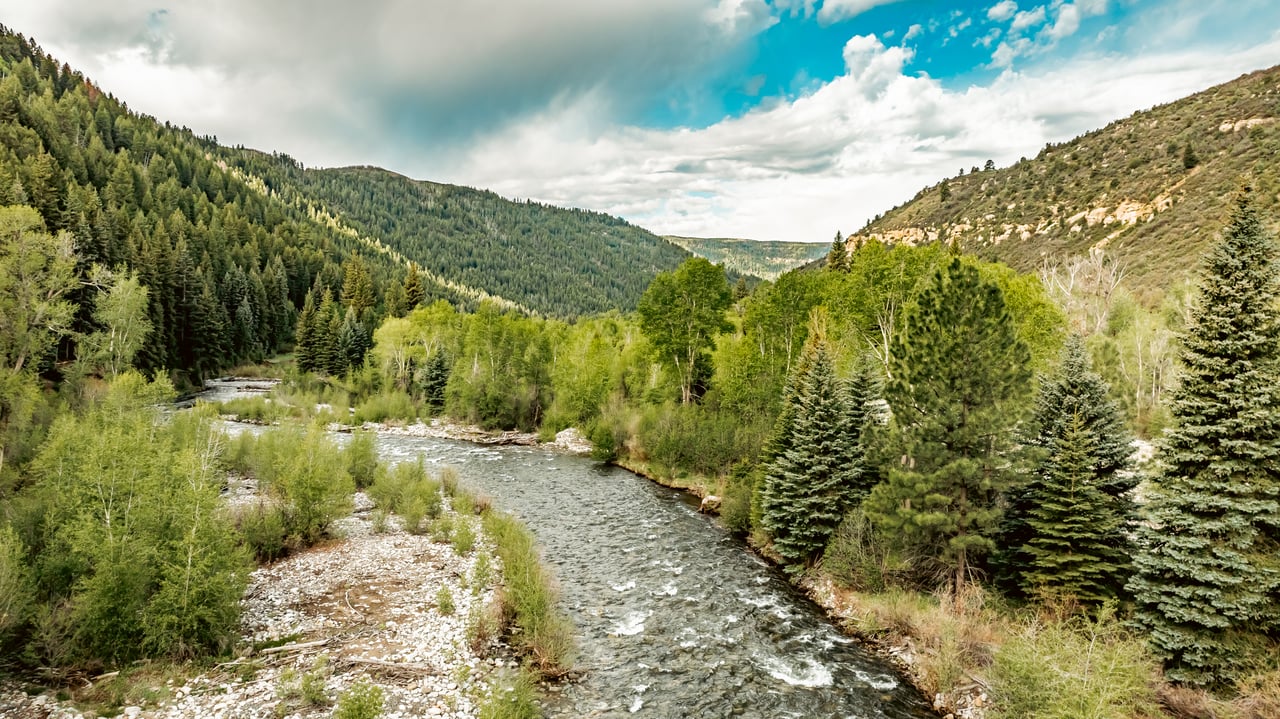 River winding through a forested mountain valley with rocky banks and evergreen trees.
