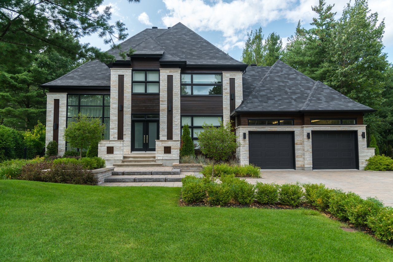 Modern stone-and-wood home with a two-car garage, landscaped beds, and a broad front lawn.
