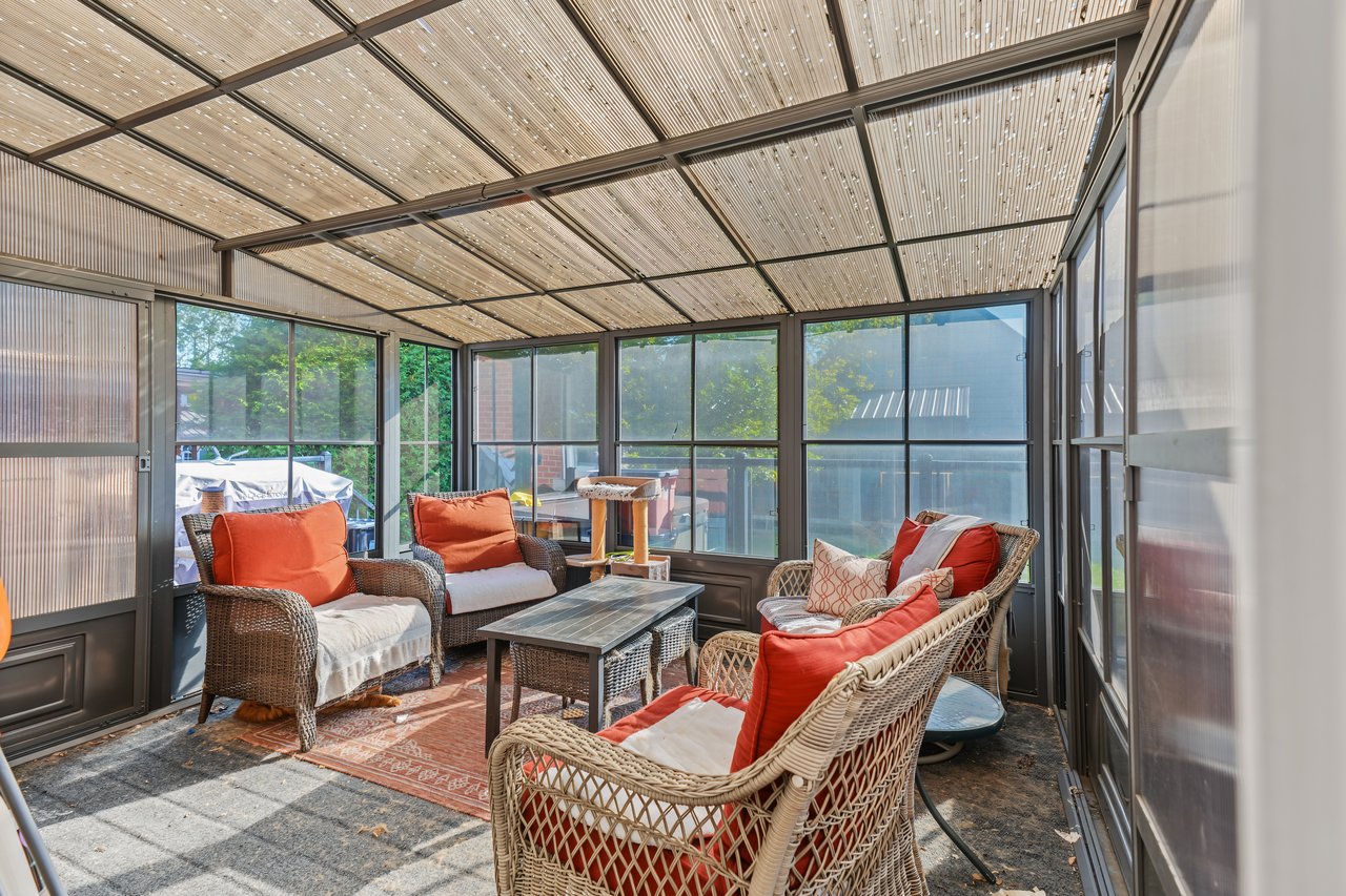 Sunroom with wicker seating, bright red and orange cushions, and floor-to-ceiling windows.