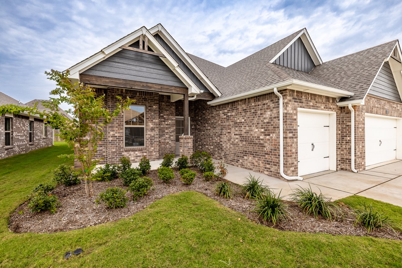 Brick house with two white garage doors, a covered entry, and landscaped front lawn.