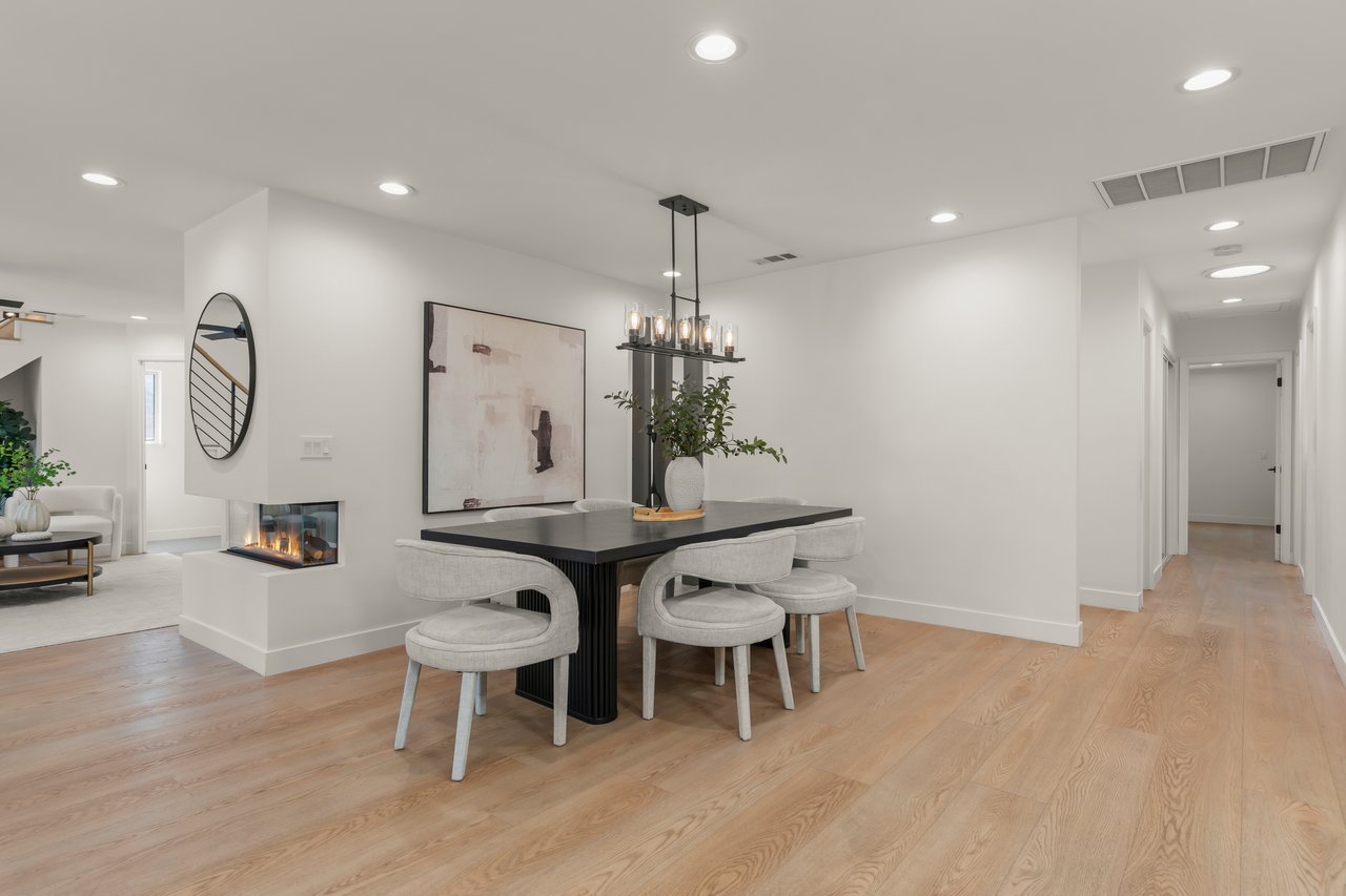 Dining area with a black table, upholstered chairs, and a two-sided fireplace.