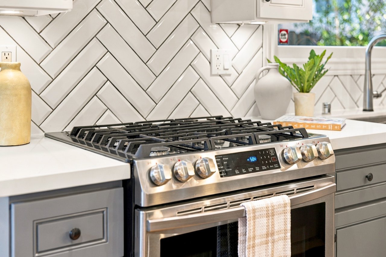 Kitchen with a stainless steel gas range, white herringbone backsplash, and gray cabinets.