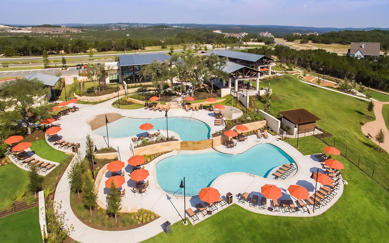 Neighborhood pool complex with two pools, orange umbrellas, and a clubhouse