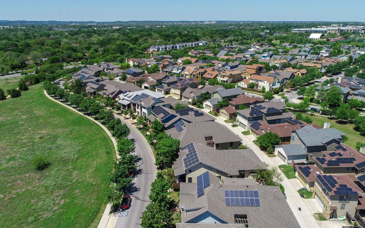 Aerial view of a solar-panel-dotted neighborhood beside a broad greenbelt.