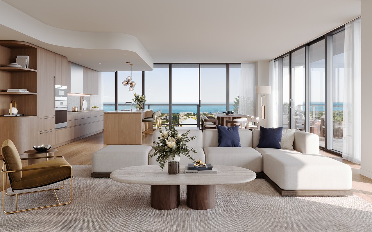 Open-plan condominium living room with pale wood kitchen, white sectional sofa, and ocean views.