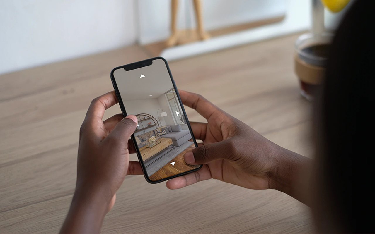 Hands use a smartphone to view a virtual tour of a furnished living room.