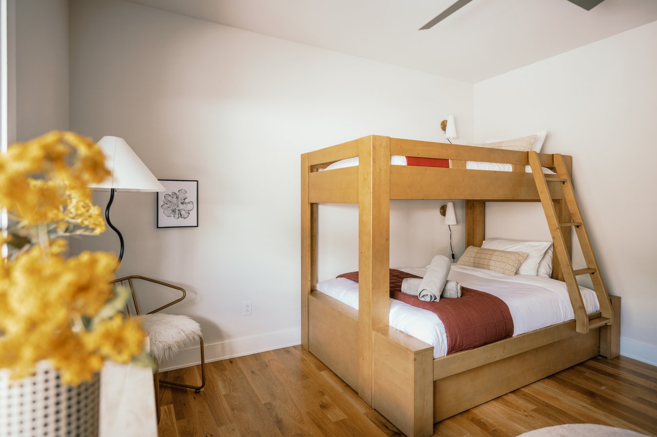 Bedroom with a wooden bunk bed, white bedding, rust-colored throws and warm wood floors.