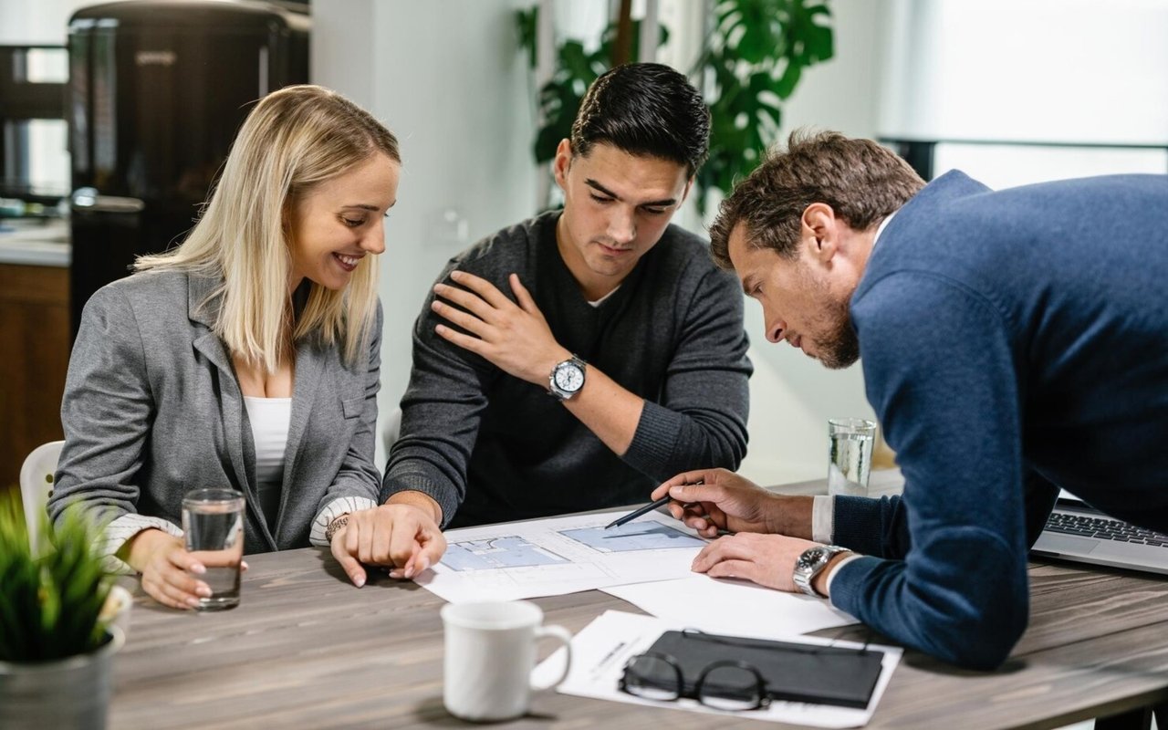 Three people review floor plans and paperwork together at a table.