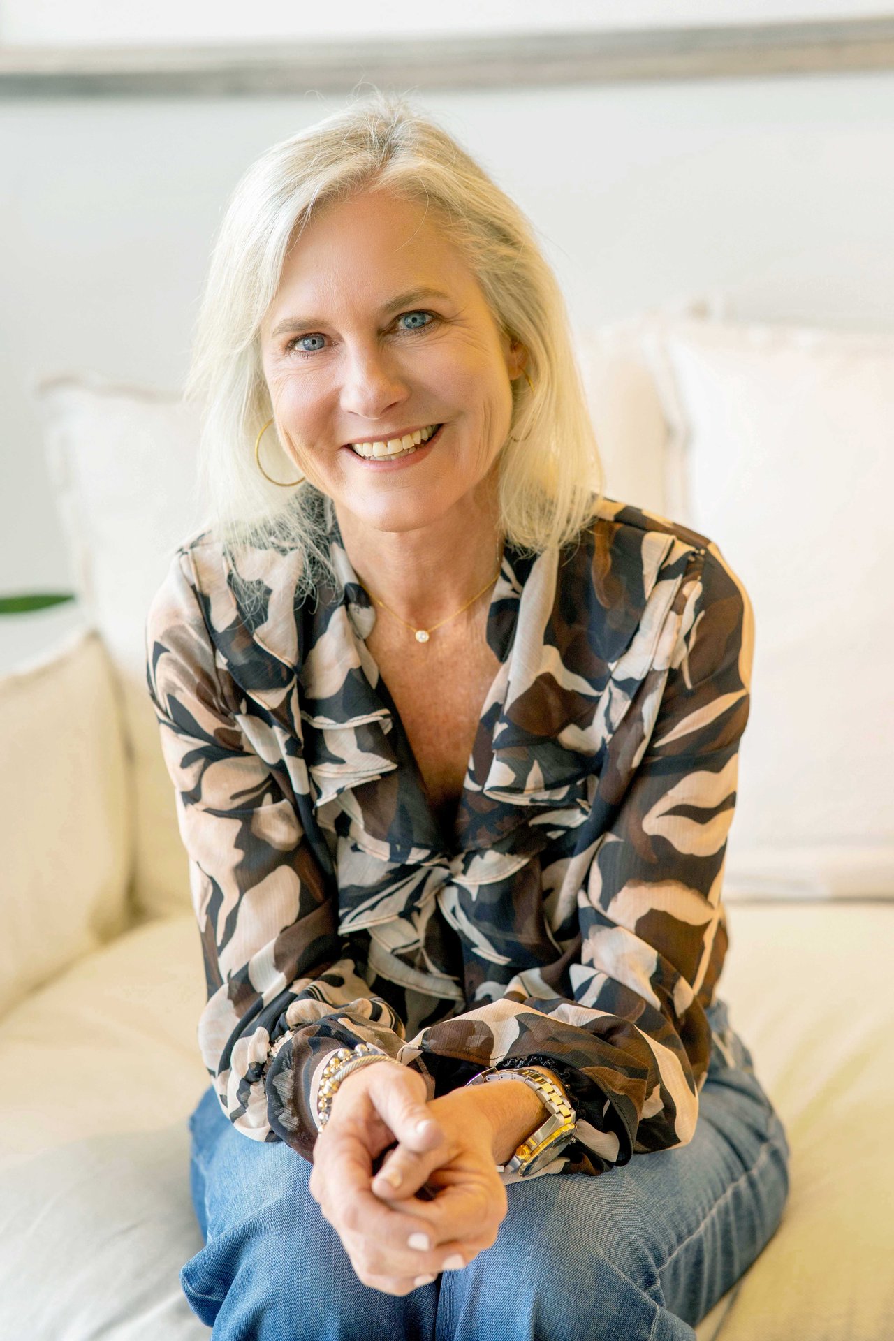 Janeen Anderson seated and smiling in a patterned blouse and jeans.