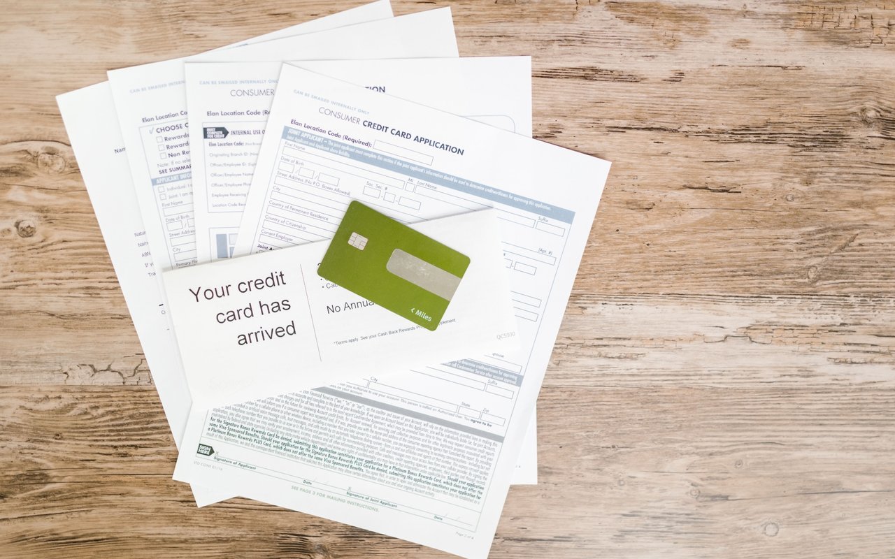 Green credit card on a credit card application and welcome letter atop a weathered wooden table.