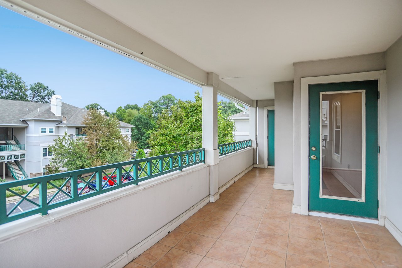 Covered condo balcony with tan tile, teal railings, and a teal glass-panel door.