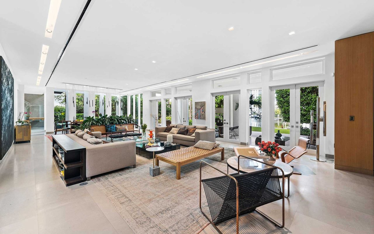 Modern living room with neutral sofas and floor-to-ceiling windows overlooking greenery and water.