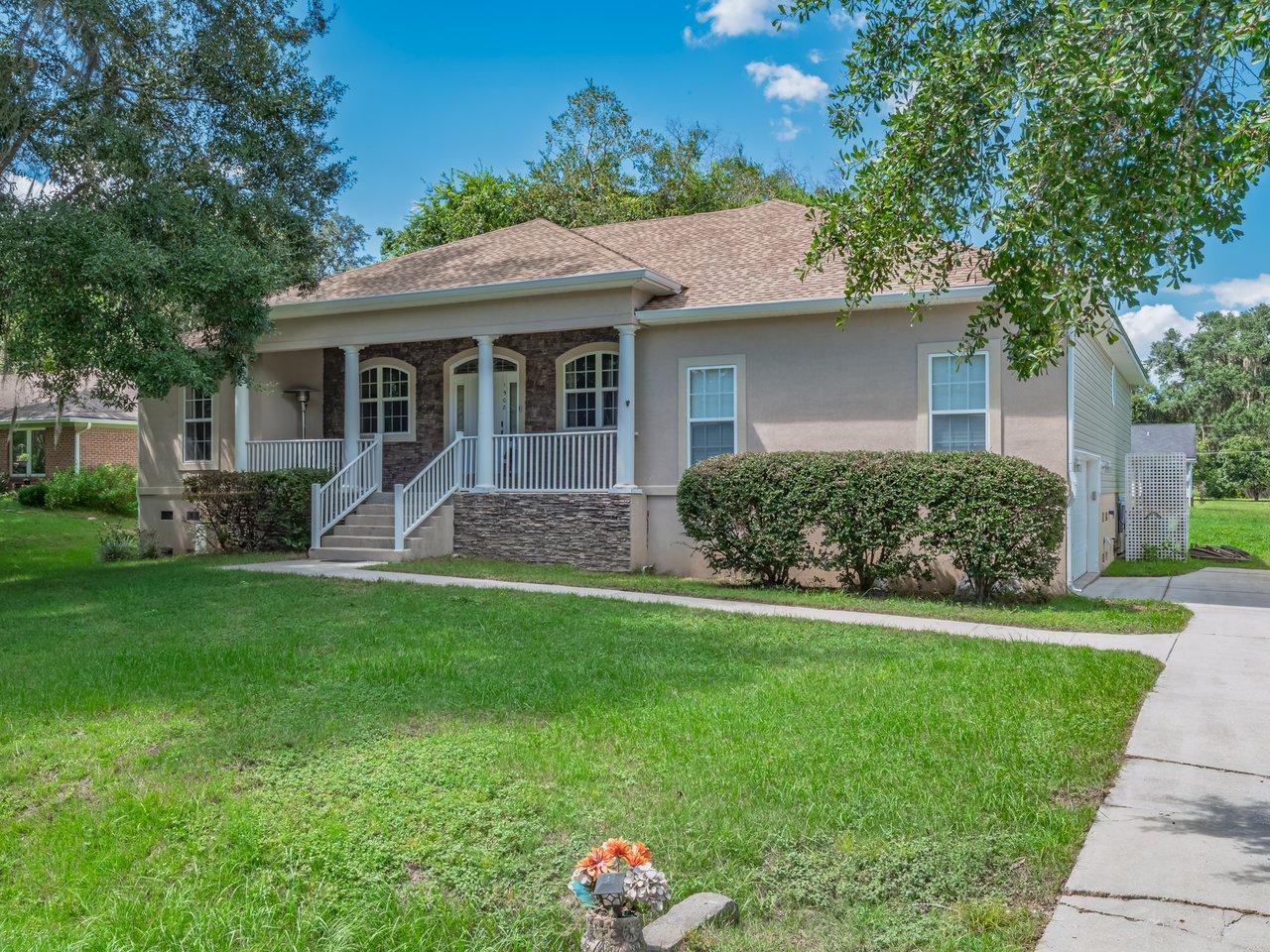 Single-story home with a stone-accented front porch, white railings, and a broad green lawn.