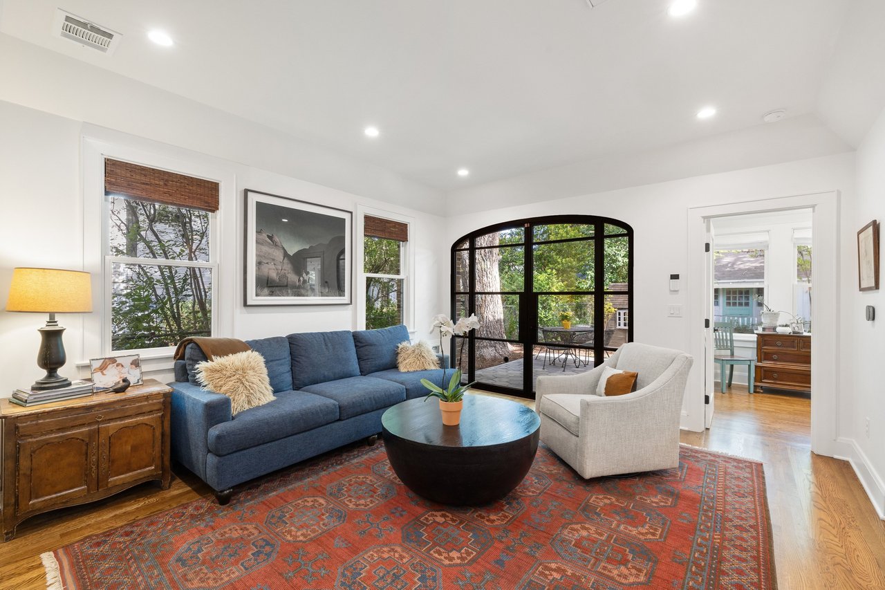 Living room with a blue sofa, patterned rug, and arched glass doors overlooking a leafy patio.
