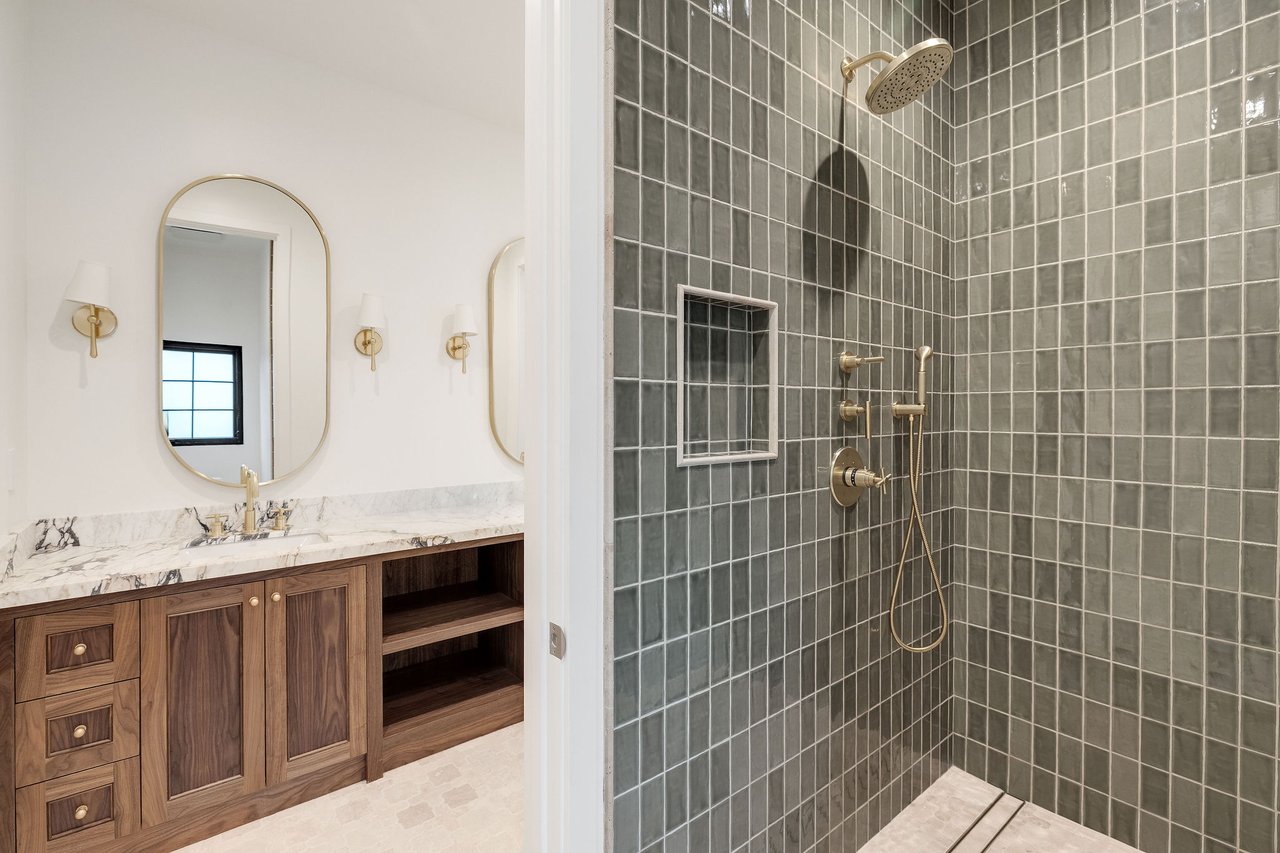 Bathroom with a gray-tiled walk-in shower, brass fixtures, and a marble-topped wood vanity.