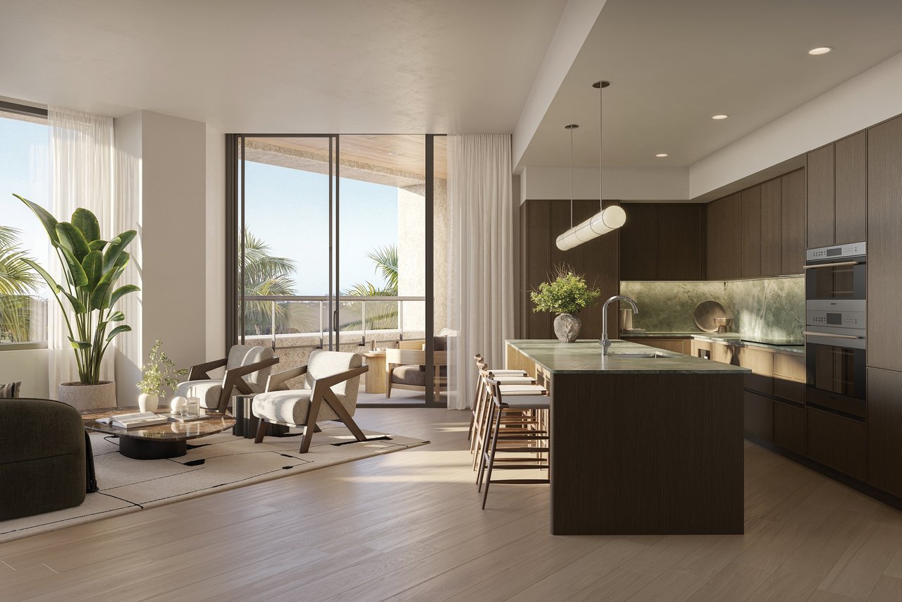 Open-plan kitchen and living area with a large stone island and palm trees visible through tall windows.
