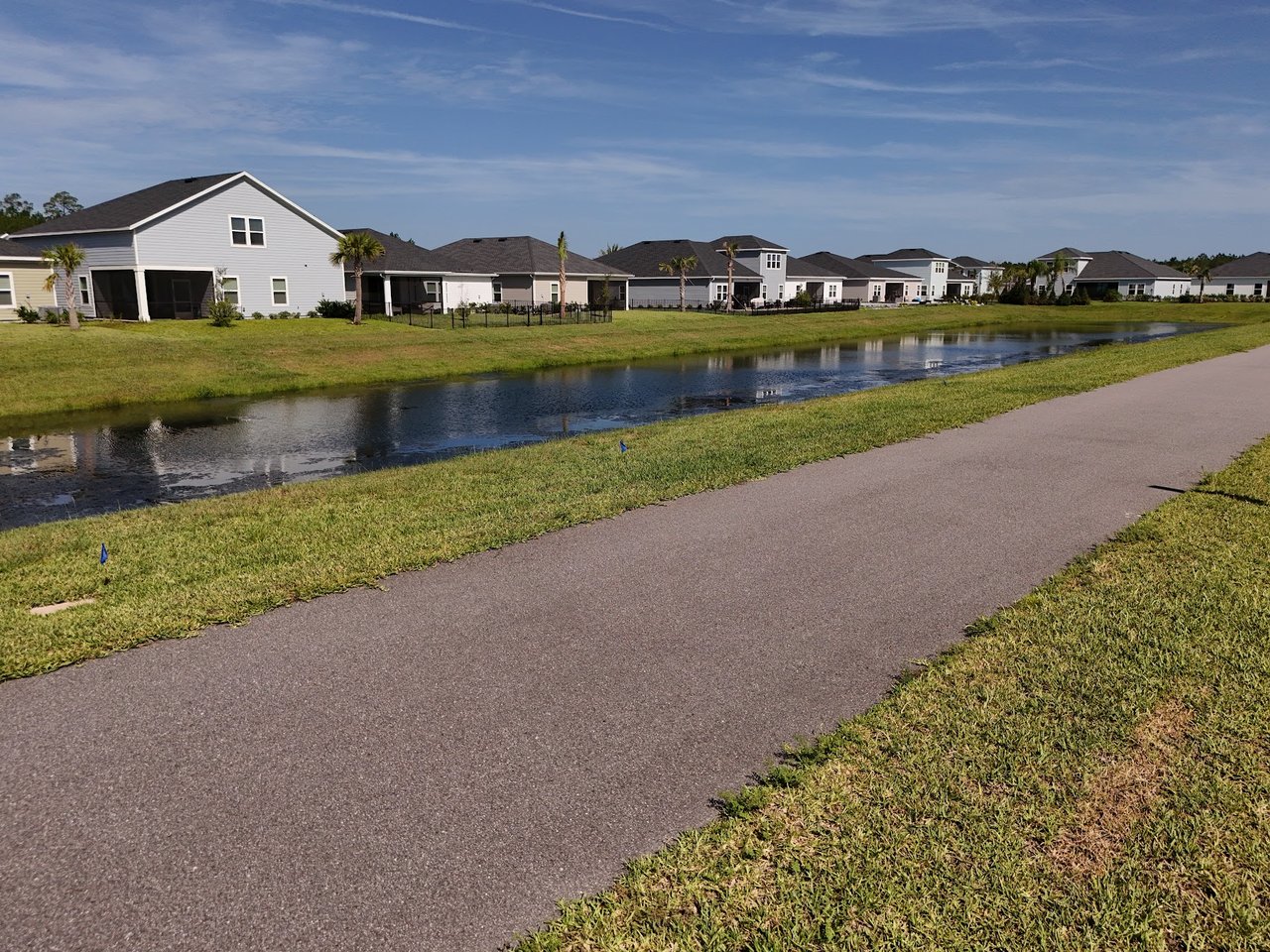 Detached homes line a grassy canal beside a paved path.