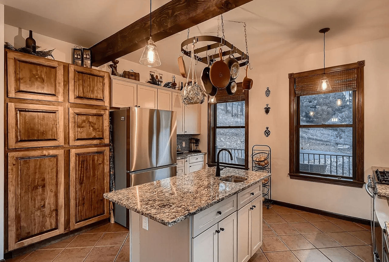 Kitchen with rustic wood cabinets, a granite island, hanging cookware, and windows overlooking a porch.