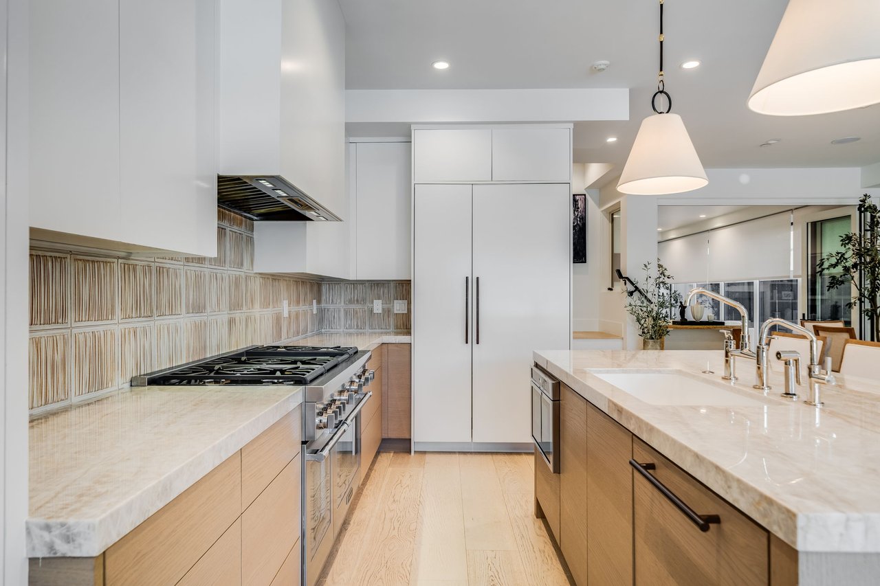Modern kitchen with marble counters, white cabinetry, a stainless steel gas range, and pendant lights.