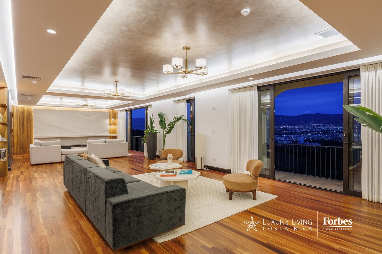 Penthouse living room with hardwood floors and floor-to-ceiling windows overlooking the city at night.