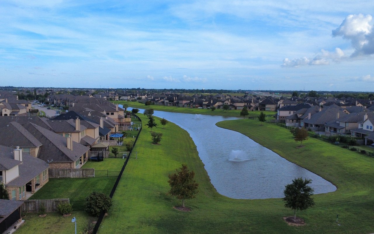 Aerial view of homes around a pond with grassy banks and a fountain.