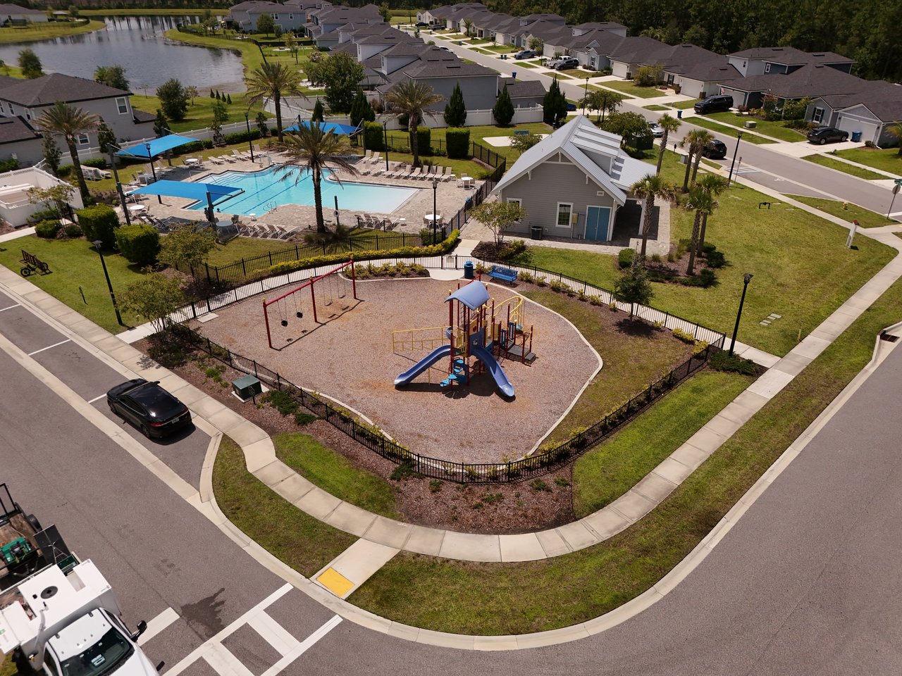 Aerial view of a neighborhood playground and pool beside a pond and homes.