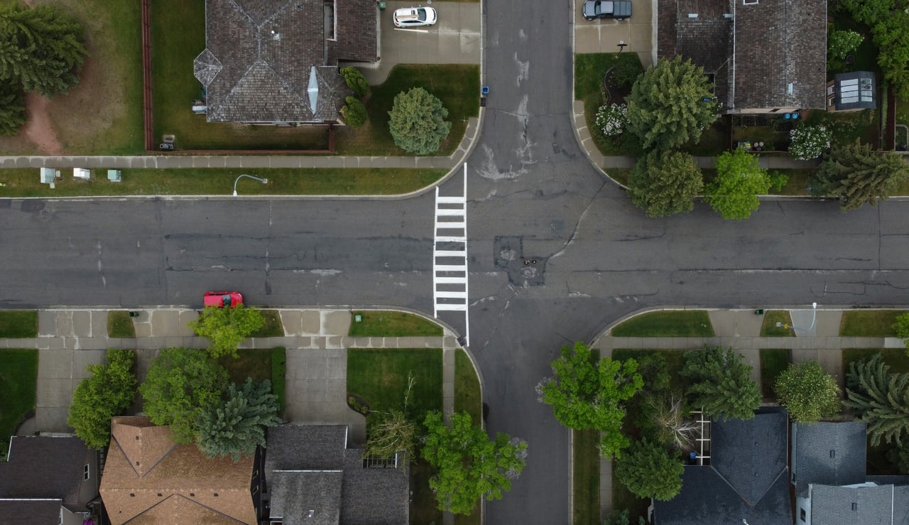 Aerial view of a tree-lined residential neighborhood intersection with homes and sidewalks in Utah County