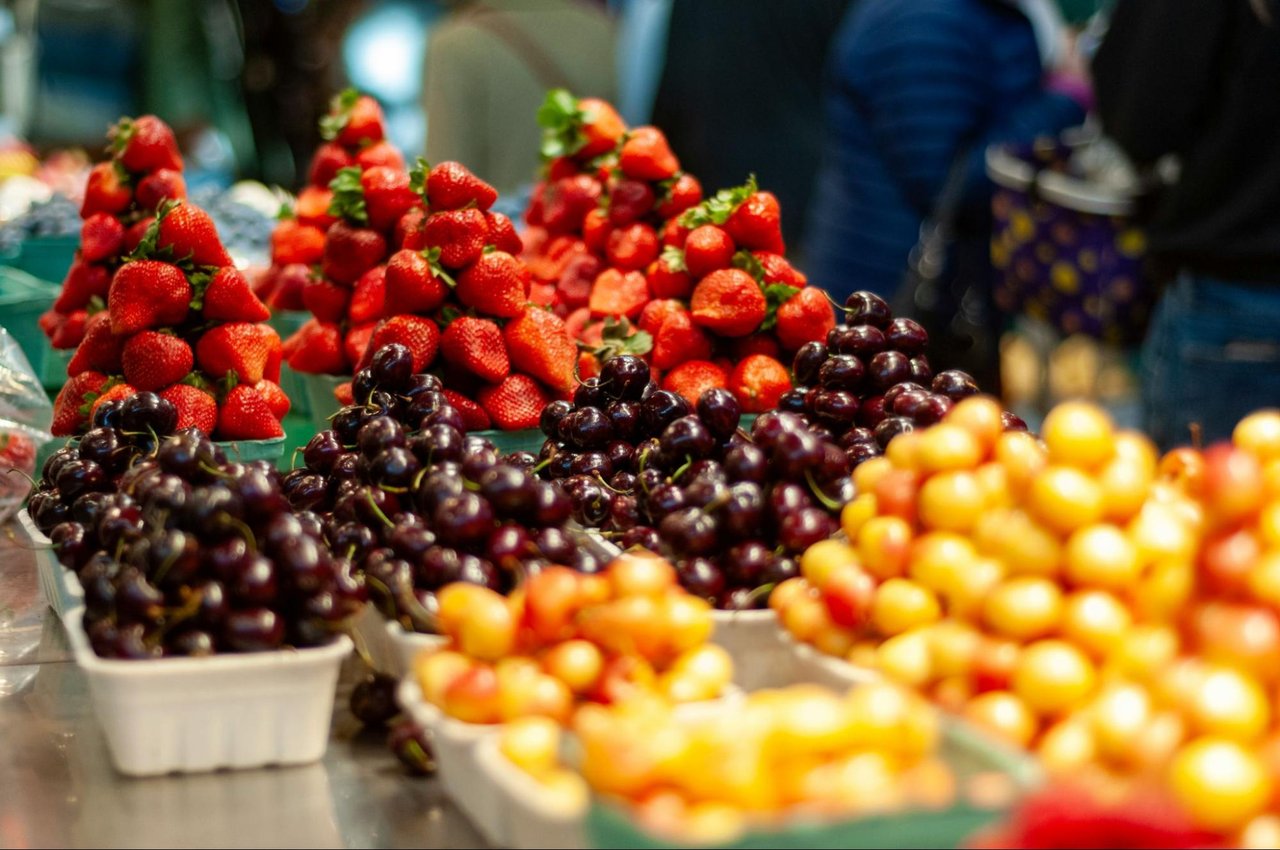 Strawberries, dark cherries, and yellow-orange fruit arranged in trays at a market stall.