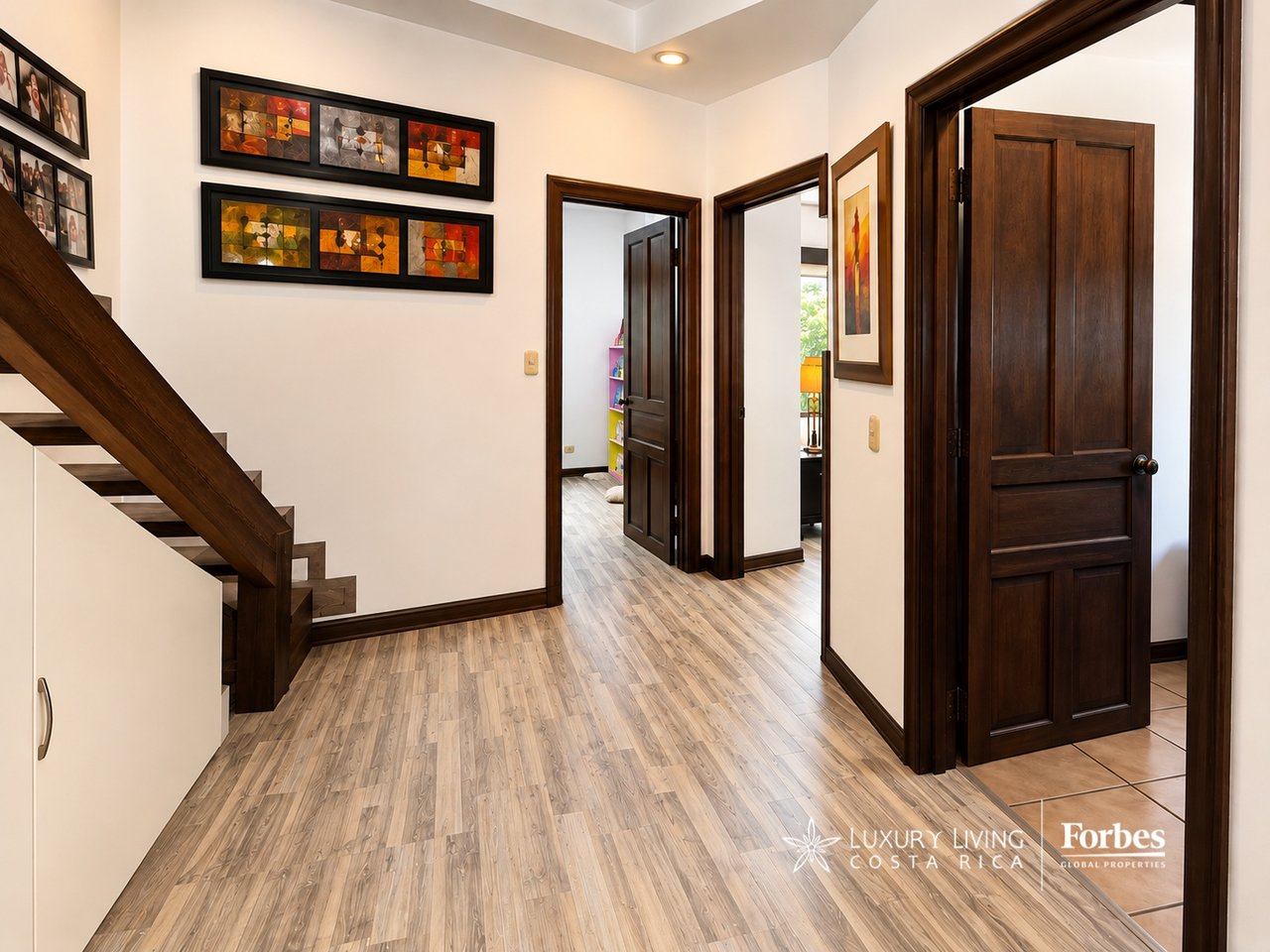 Hallway with a dark wood staircase, framed artwork, and several open doorways.
