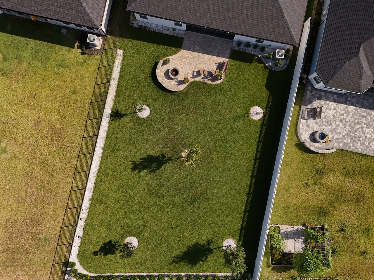 Aerial backyard view with a large lawn and curved stone patio with fire pit and chairs.