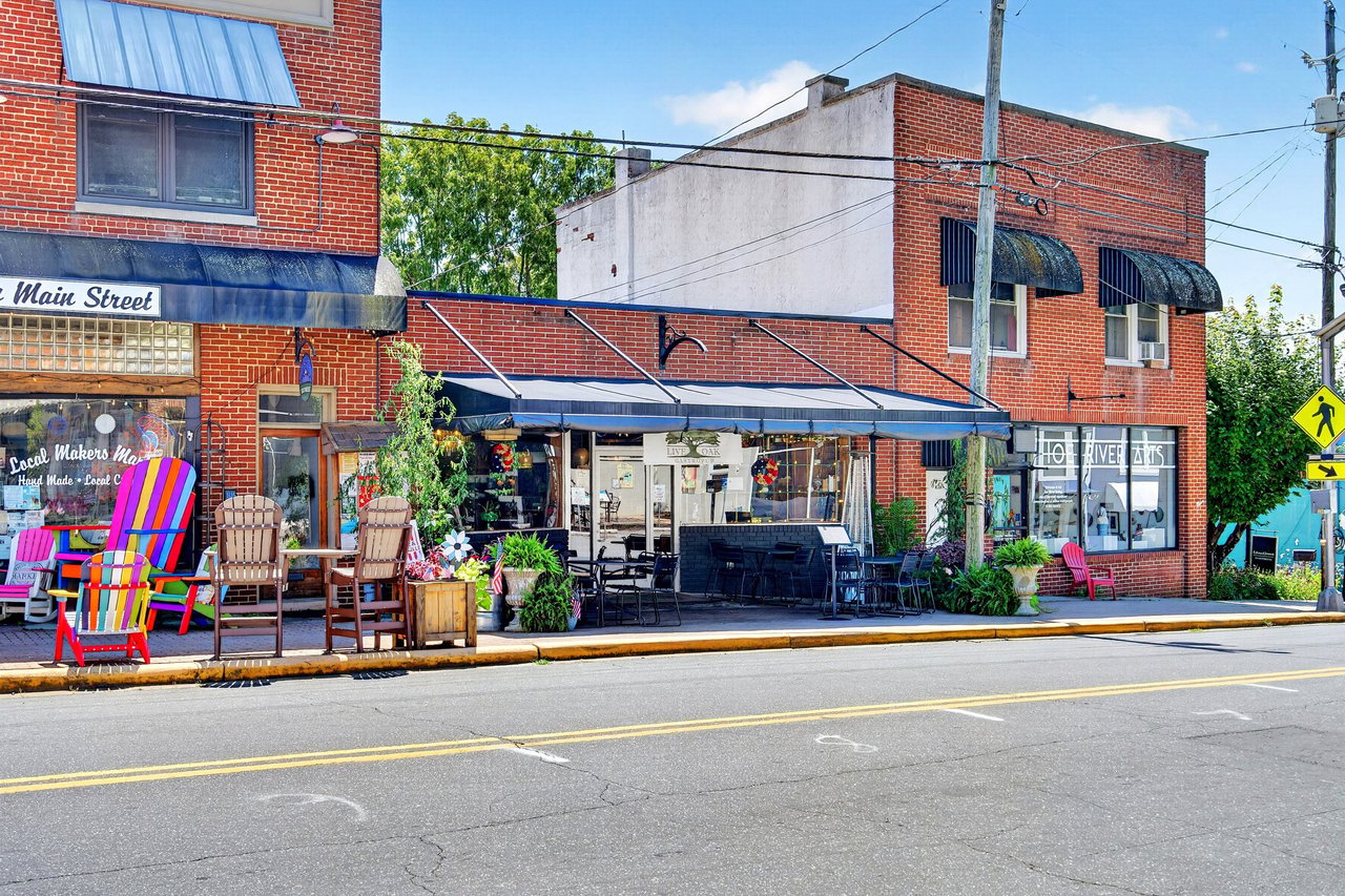 Red-brick Main Street storefront with blue awnings and outdoor patio seating.
