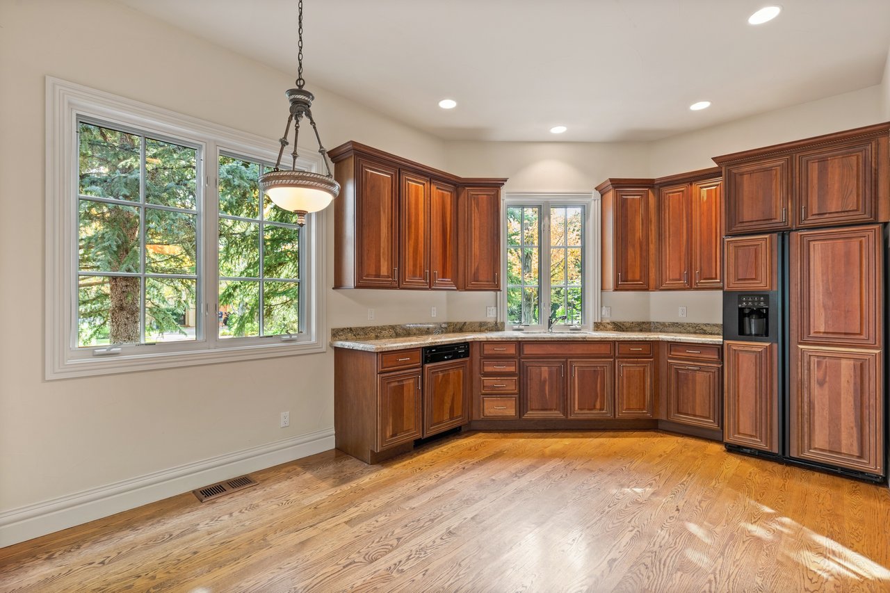 Kitchen with cherry cabinets, granite countertops, hardwood floors, and large windows overlooking trees.