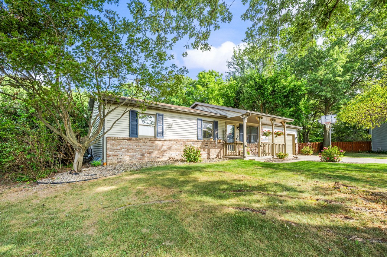Single-story ranch home with a covered porch, brick facade, leafy yard, and basketball hoop.