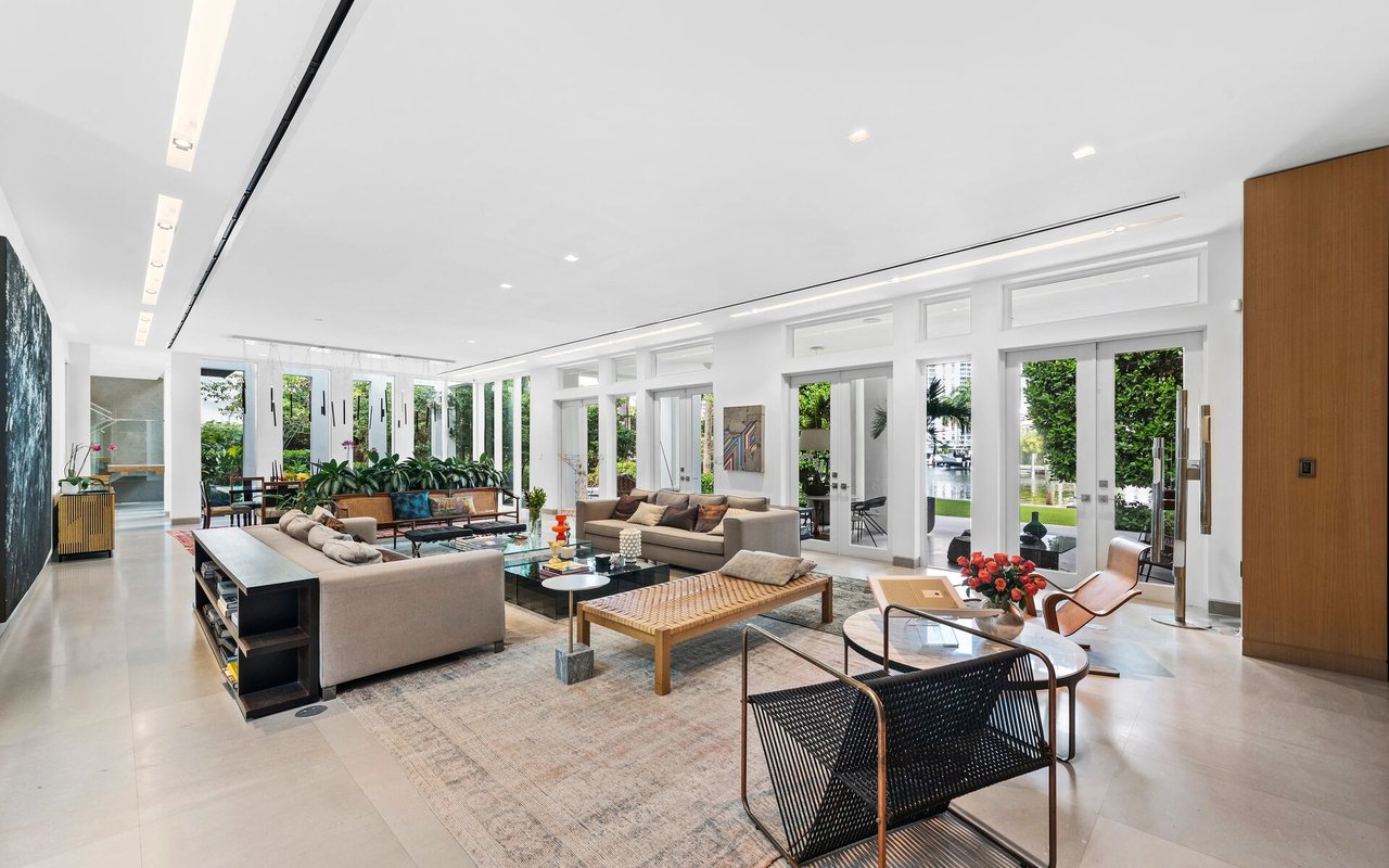 Modern living room with multiple seating areas and tall glass doors overlooking a garden and water.