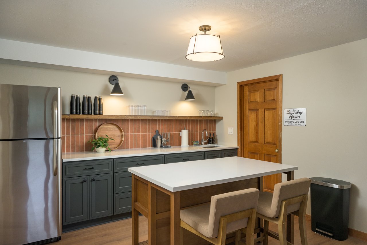 Kitchen with dark gray cabinetry, terracotta tile backsplash, stainless refrigerator, and white island.
