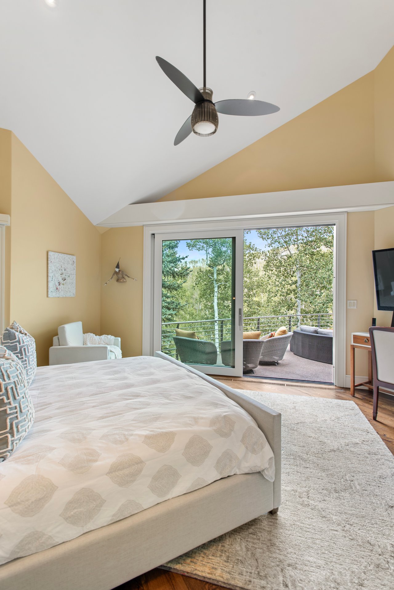 Bedroom with a vaulted ceiling and sliding doors opening to a tree-lined balcony.