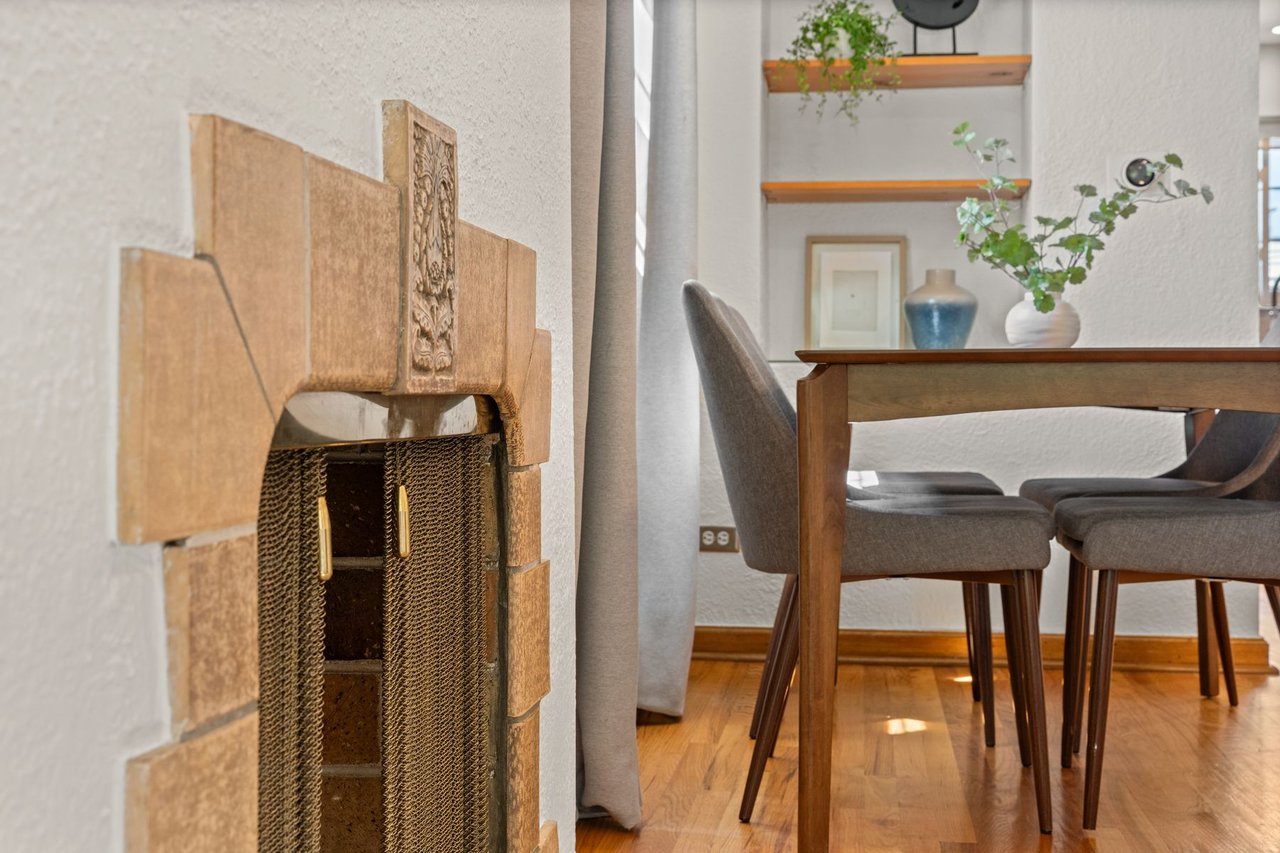Dining area with a carved stone fireplace, wooden table, gray chairs, and hardwood floors.