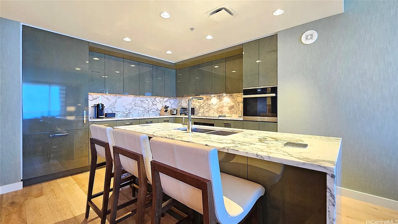 Modern condo kitchen with a large marble island, dark cabinetry, built-in appliances, and upholstered bar stools.