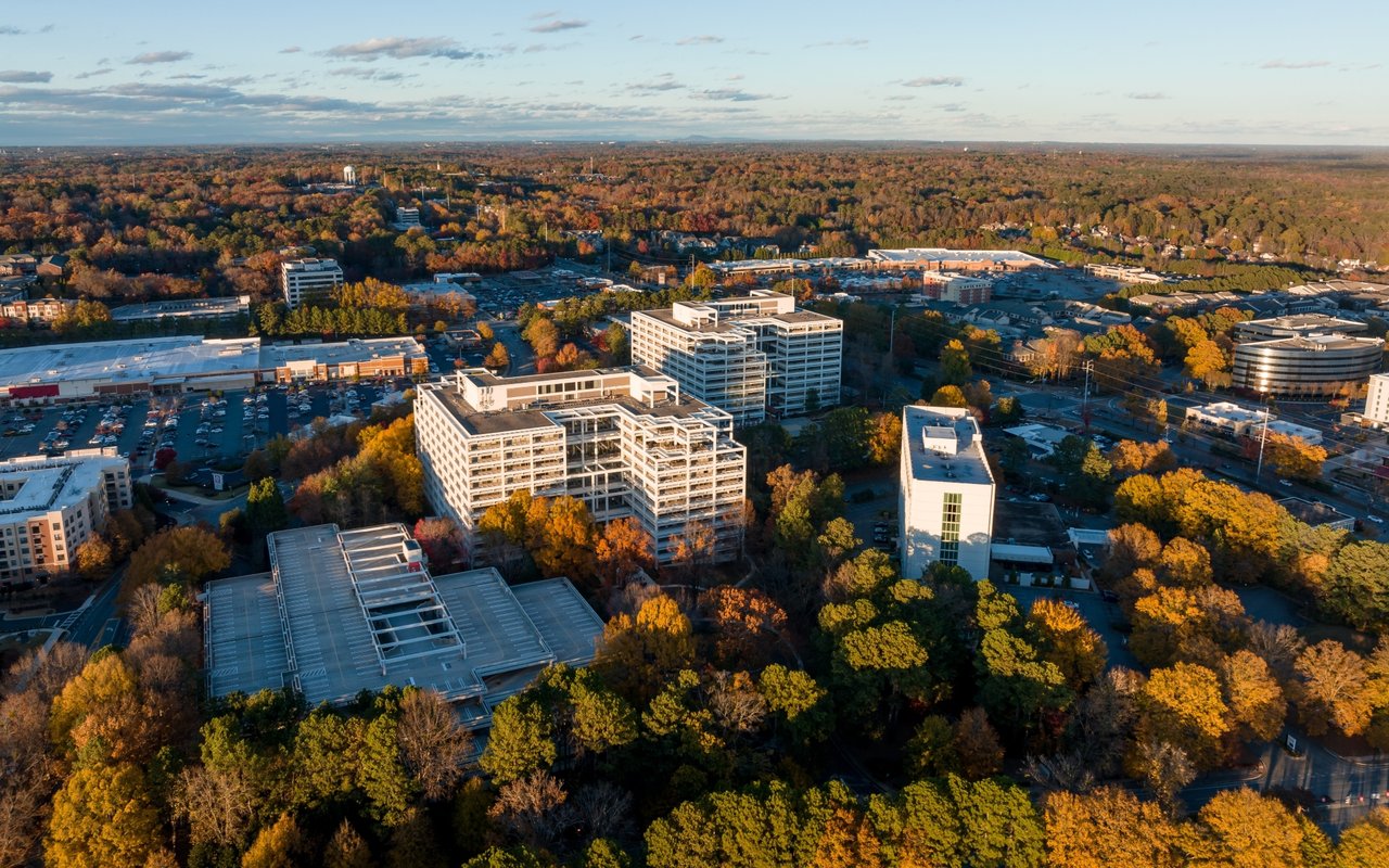 Aerial view of office buildings and parking lots amid autumn-colored trees.