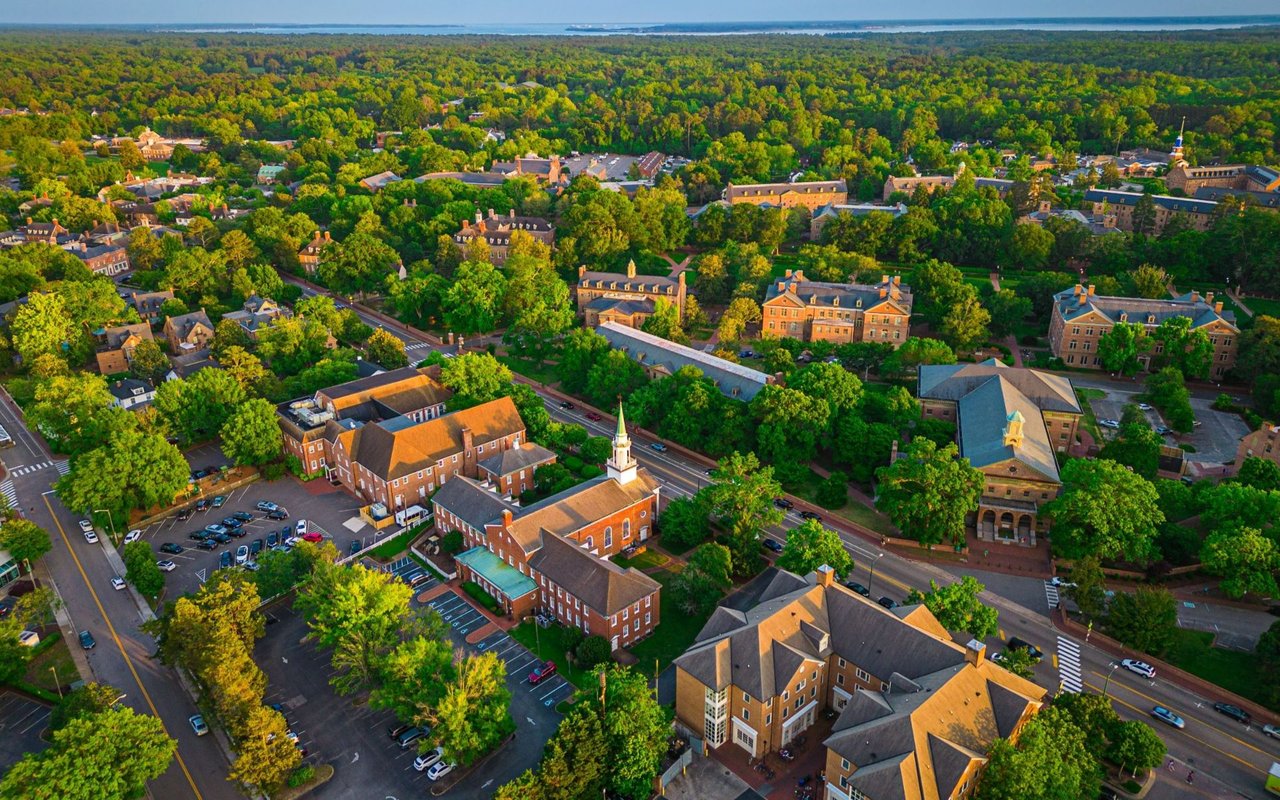Aerial view of Williamsburg’s brick buildings and tree-lined streets, with water visible in the distance.