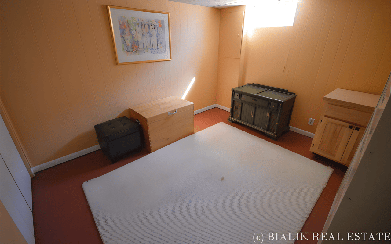 Furnished room with paneled walls, a large white rug, storage chests, and framed artwork.