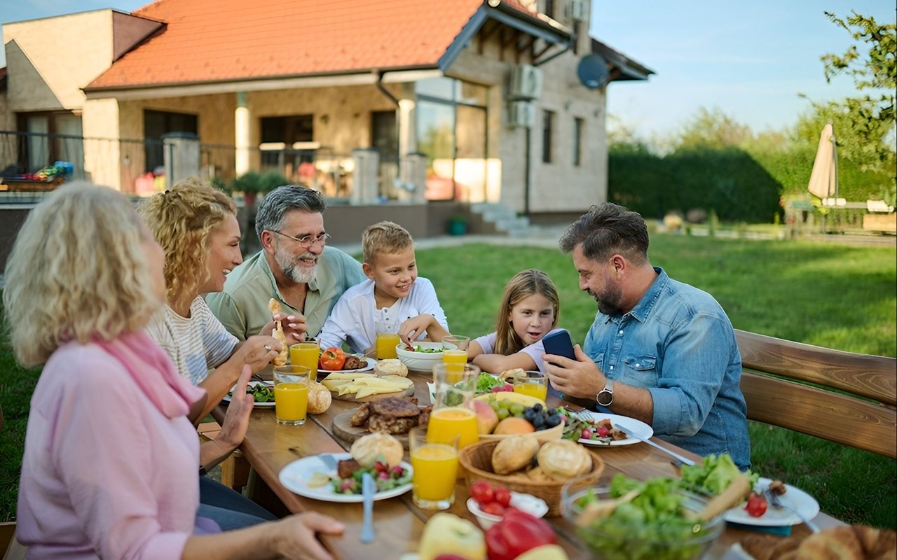A multigenerational family shares an outdoor meal beside a house.