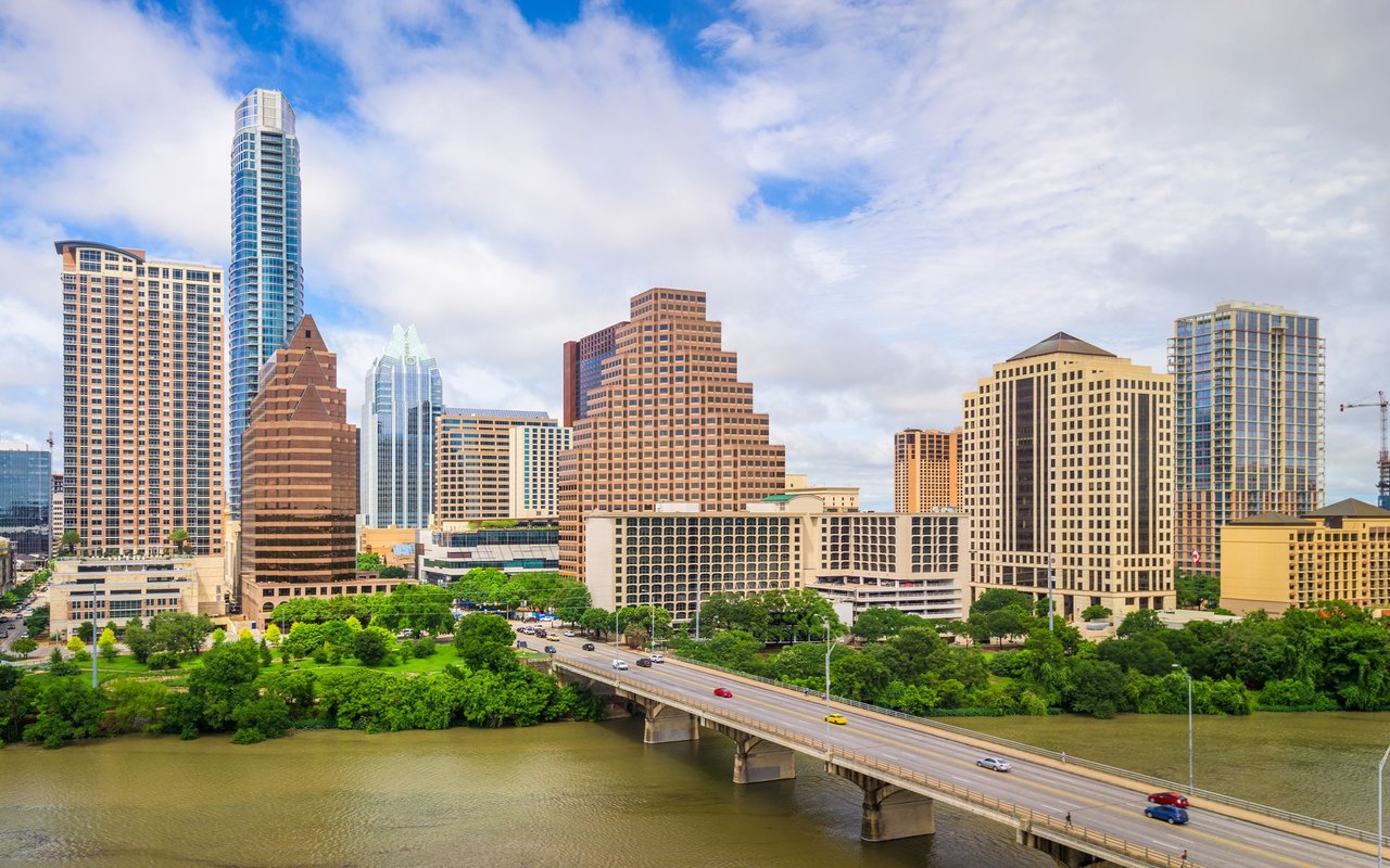 Downtown Austin skyline along the river, with a highway bridge in the foreground.