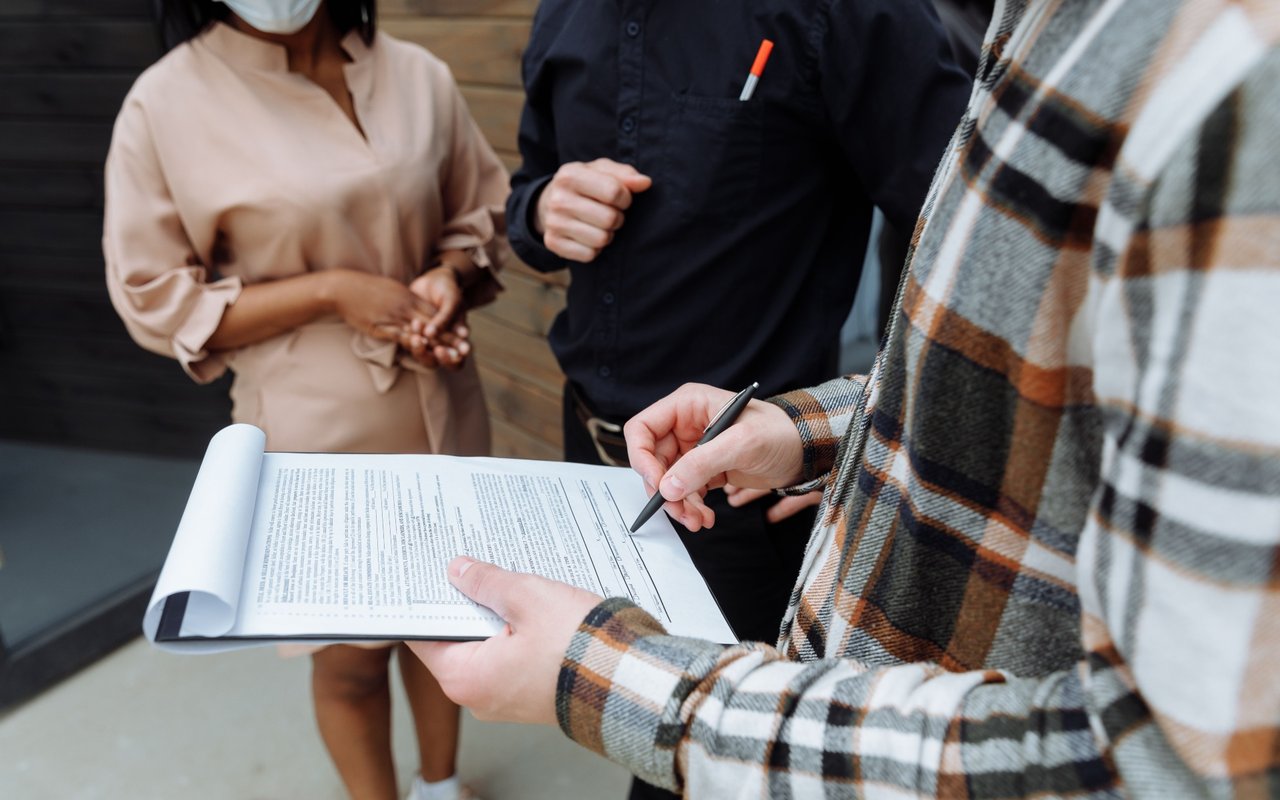 People review a real estate agreement as one person points to a line with a pen.