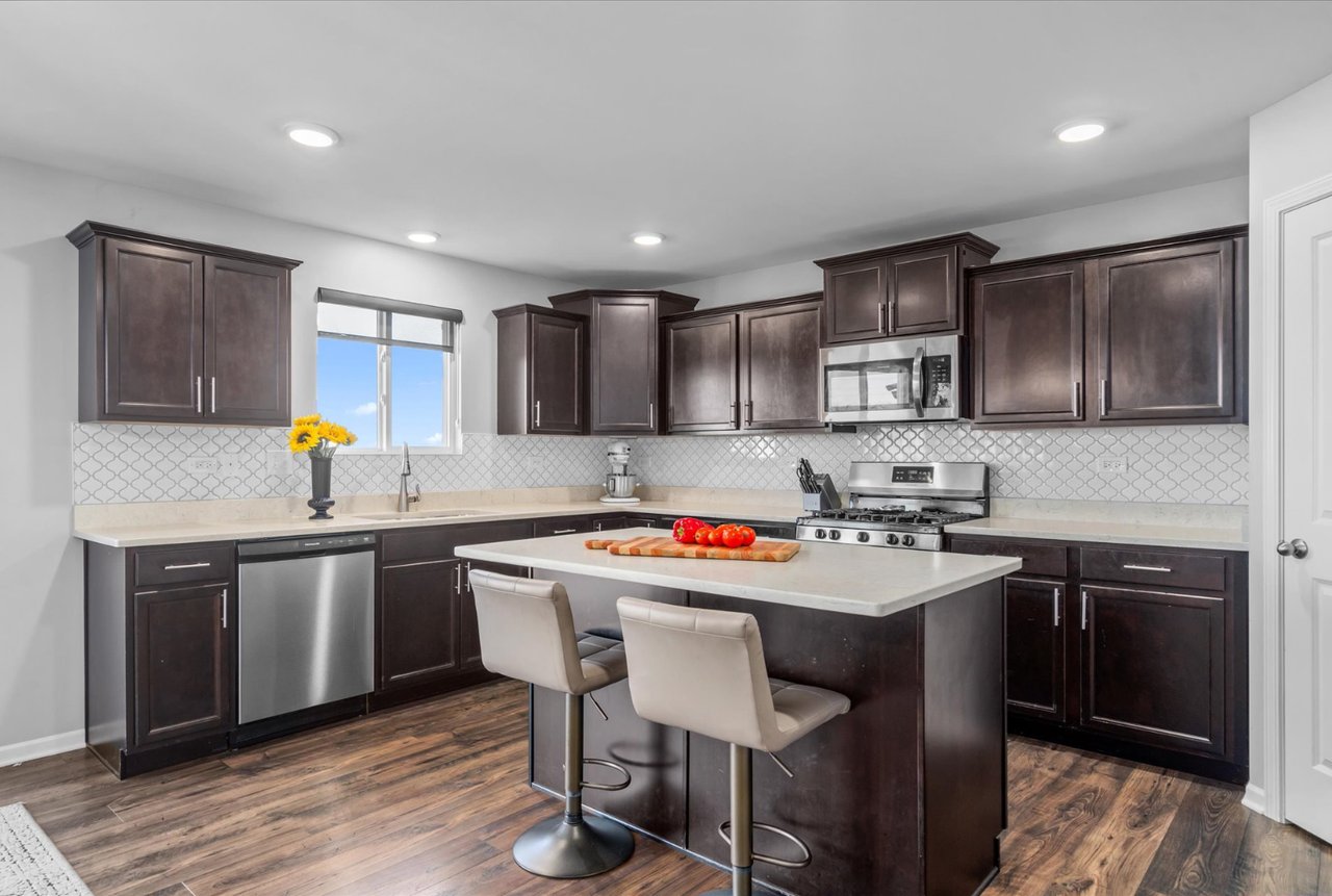 Staged Tully Team kitchen with espresso cabinets, sunflowers, leather stools, and red tomatoes on a wood cutting board.