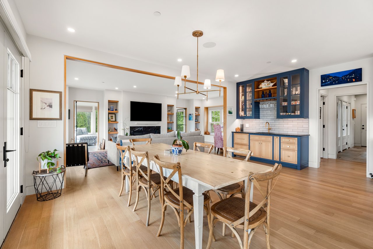 Open-plan dining room with a long wood table, blue kitchen cabinetry, and living room beyond.
