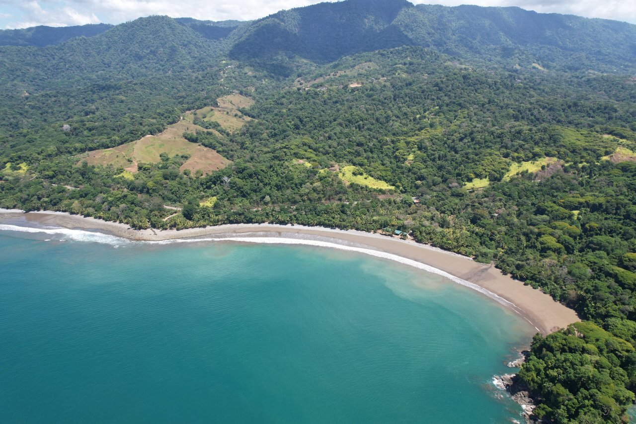 Curved tropical beach and turquoise water below forested hills and mountains.