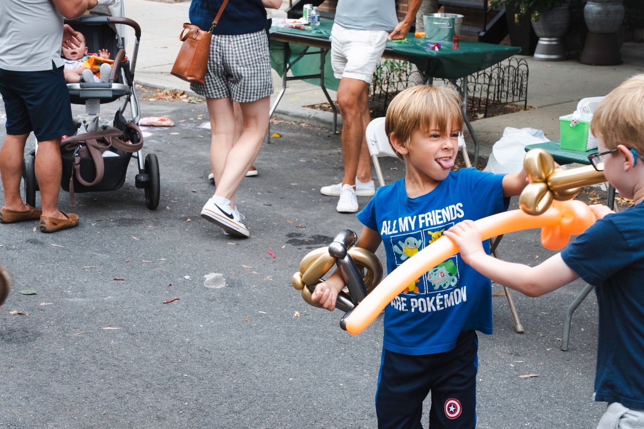 Children play with balloon animals at an outdoor neighborhood block party.